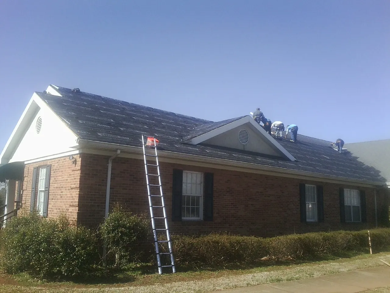 Crew tearing shingles off a brick ranch roof with a ladder set — Metal Roof Repair work by our crew in Coal City