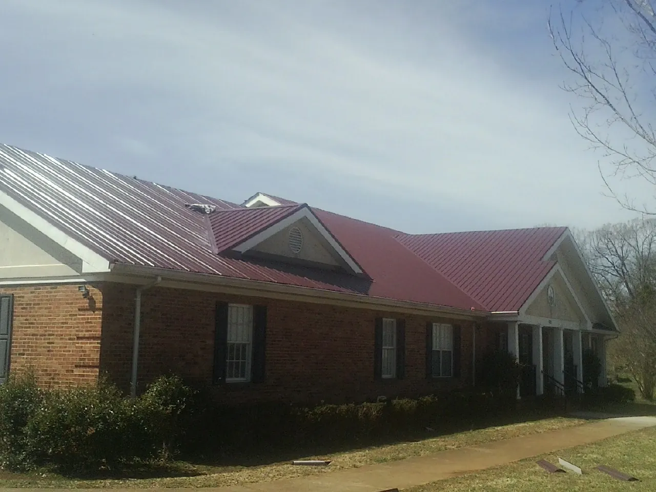 Red metal roof with gabled entries on a long brick building, from a Hail Damage Roof Repair job in Coal City