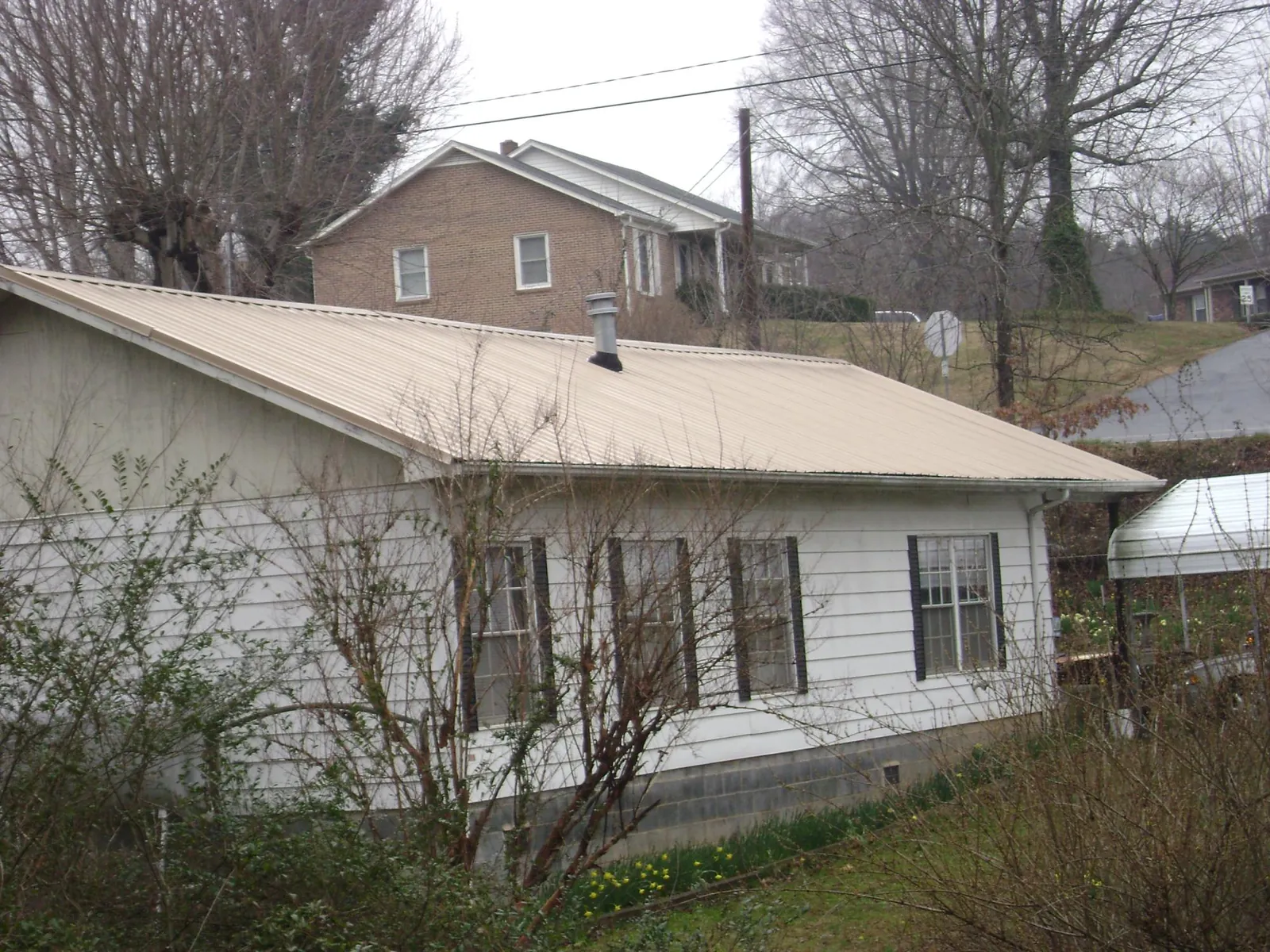Tan metal roof on a white sided house set into a hillside — Commercial Roofing by Roofing Brothers in Coal City
